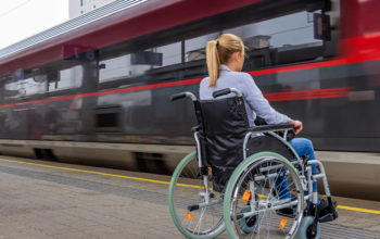 На фото девушка сидит в инвалидном кресле, а рядом проезжает железнодорожный поезд