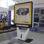 На фотографии изображен большой вертикальный экран, в котором отображается тактильно-графическая мнемосхема Новоторжского Борисоглебского монастыря, установленный на выставочном стенде Тифлоцентра "Вертикаль" на Международной выставке Интеграция-2026.