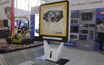 На фотографии изображен большой вертикальный экран, в котором отображается тактильно-графическая мнемосхема Новоторжского Борисоглебского монастыря, установленный на выставочном стенде Тифлоцентра "Вертикаль" на Международной выставке Интеграция-2026.
