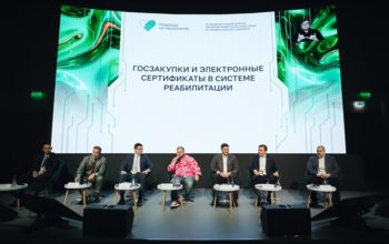 На фотографии запечатлена панельная дискуссия на официальном мероприятии, где на сцене в ряд сидят семеро мужчин-спикеров в костюмах, среди которых выделяется один участник в яркой розовой рубашке с цветочными мотивами. На заднем плане расположен огромный экран с надписью «ГОСЗАКУПКИ И ЭЛЕКТРОННЫЕ СЕРТИФИКАТЫ В СИСТЕМЕ РЕАБИЛИТАЦИИ», логотипом «Надежда на технологии» и окном трансляции с сурдопереводчиком.