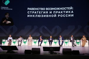 На фотографии представлена панельная дискуссия в рамках форума «Надежда на технологии», где на сцене сидят спикеры в деловых костюмах. Над ними расположен большой темный экран с крупной надписью «РАВЕНСТВО ВОЗМОЖНОСТЕЙ: СТРАТЕГИЯ И ПРАКТИКА ИНКЛЮЗИВНОЙ РОССИИ» и небольшим окошком с сурдопереводчиком в левом верхнем углу.