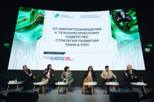 На фотографии запечатлена панельная дискуссия форума «Надежда на технологии», где на сцене сидят шестеро экспертов на фоне большого светлого экрана с надписью «ОТ ИМПОРТОЗАМЕЩЕНИЯ К ТЕХНОЛОГИЧЕСКОМУ ЛИДЕРСТВУ: СТРАТЕГИЯ РАЗВИТИЯ РЫНКА ПРН», логотипом партнера сессии «Деловая Россия» и окошком сурдопереводчика.