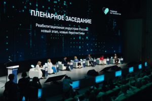 На фотографии зал пленарного заседания форума в 2025 году. На сцене сидят спикеры и готовятся к выступлению.